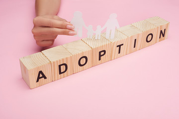 cropped view of woman holding paper cut gay family on wooden cubes with adoption lettering on pink...