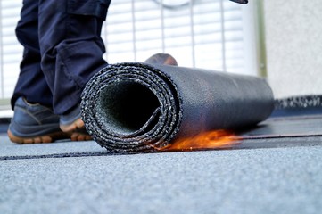 Flat roof installation with propane blowtorch during construction works with roofing felt. Heating and melting bitumen roofing felt. Roofing felt. Roofer working. Roofer working tool. Waterproofing - obrazy, fototapety, plakaty