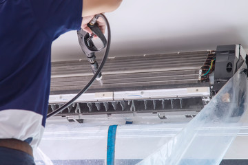 The technicians are cleaning the air conditioner by spraying water. Hand and water spray are cleaning the air conditioner. Focus at air conditioner.