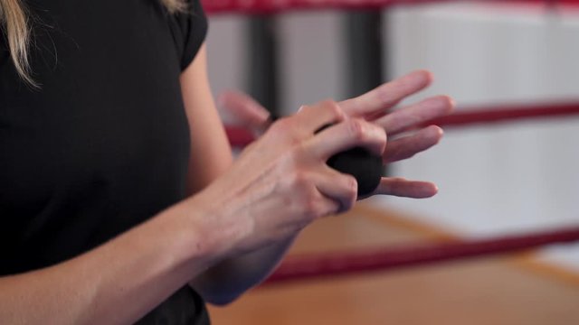 Close-up of a professional female boxer wearing black hand strap on wrist before training. Boxing practice in gym. Female professional sport concept