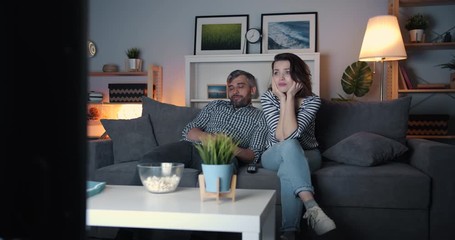 Young couple man and woman watching boring film on TV at home at night yawning relaxing on couch together with bored faces. People, house and television concept.