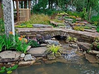 Fototapeta na wymiar A sandstone rock and water garden with a stone bridge, waterfalls and mixed planting of flowers
