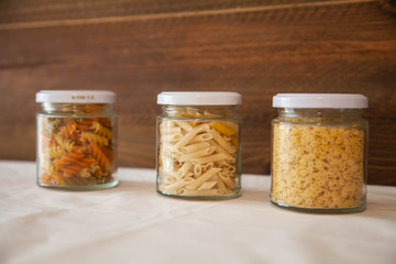 glass jars filled with italian pasta with wooden background