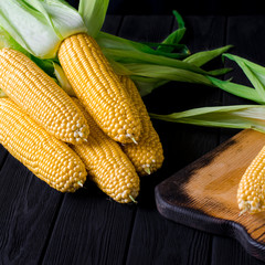 Yellow juicy corn with green leaves on a black tree table