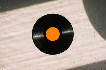 Obraz premium Vinyl record on a white background. Sunlight is falling on a black round disk and background. Musical style, analog sound. Retro style
