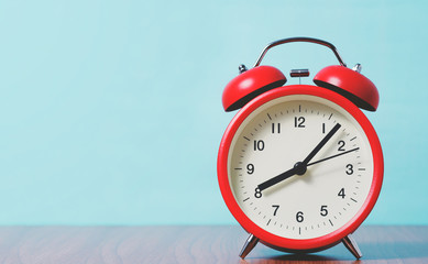 Red alarm clock with 8 O'clock on wooden table and blue background, retro style color.