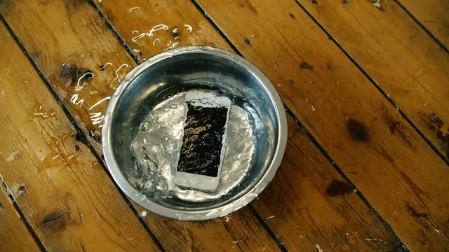 iPhone falling into a dog bowl making a massive splash of water on the wood floor accidents happen, frustrated business man, soaking wet broken phone, big mistake insurance claim for this mobile phone