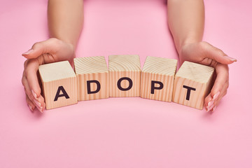 partial view of woman holding wooden cubes with adopt lettering on pink background