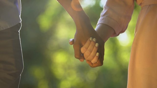 Multiracial couple holding hands at sunny park, romantic and intimacy, close-up