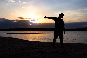 Silhouette of boy with arms spread out next to river sunset. Child on river sunset.