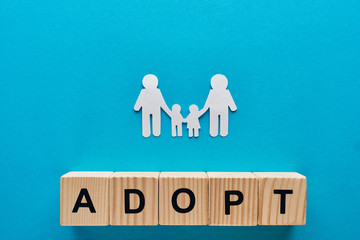 top view of paper cut gay family holding hands on blue background with adopt word on wooden cubes