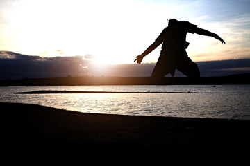 Silhouette of boy with arms spread out next to river sunset. Child on river sunset.