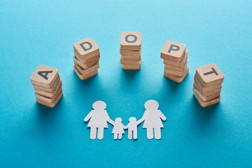 wooden blocks with adopt lettering near paper cut lesbian family on blue background
