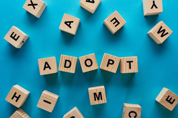 top view of adopt word made of wooden cubes on blue background