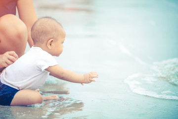 Little Asian 10 months baby excited playing the beach first time. Mother closely take care baby while playing the water.