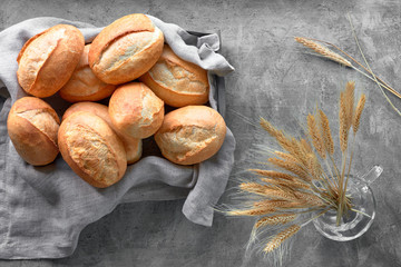 Bread buns in basket on rustic wood with wheat ears