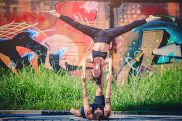 Obraz na płótnie Canvas Scenario urbano con coppia di giovani che fa acroyoga e yoga