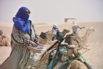 Female middle age tourist  in traditional clothes riding camel in sahara desert, Tunis. Middle age...