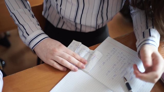 Students write in notebooks. Students use cheat sheets.  Students sit in school.