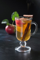 Glass of warm apple tea with lemon and cinnamon on black board. Autumn still life.