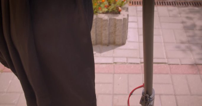 Closeup portrait of young beautiful female with long hair in glasses and dress walking with kick scooter happily outdoors