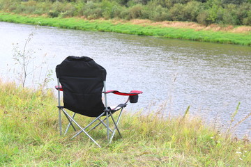 Portable folding tourist red armchair on green grass in summer on picnic near river