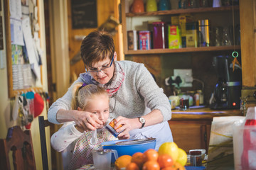 Fototapeta premium Close up lifestyle image of a young girl baking cake with her grandmother