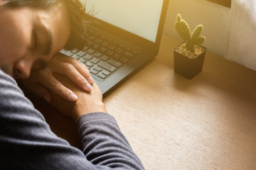 Lazy man in casual cloth is working with laptop computer by the window in the morning. The sun is shining through the window. He is a freelance programmer.