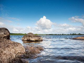 River landscape, Stones in the water blue cloudy sky reflects in river surface.