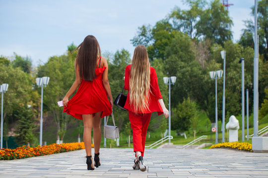 Two stylish beautiful girlfriends in red clothes walk along the promenade