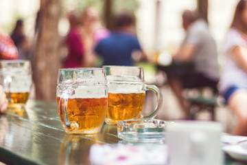 glasses of beer in garden restaurant, sitting people in background