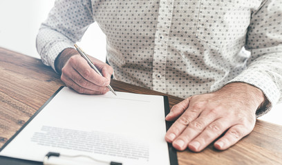 close-up of businessman sitting at wooden desk signing document or contract