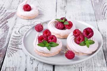 Mini Pavlova cakes topped with raspberries and mint on white wooden table