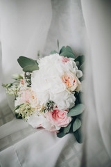 Stylish Modern wedding bouquet on white tulle in soft light in hotel room. Morning preparation before wedding ceremony. Floral arrangement for luxury event