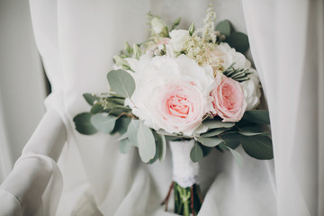 Stylish Modern wedding bouquet on white tulle in soft light in hotel room. Morning preparation before wedding ceremony. Floral arrangement for luxury event