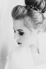 Stylish happy bride with amazing makeup posing in soft light near window in hotel room. Gorgeous sensual bride portrait. Morning preparation before wedding ceremony.