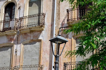 Tree leaves, lantern and old facade with colsed balconies and windows