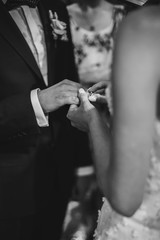 Stylish wedding couple exchanging wedding rings at holy matrimony in church. Cropped view of bride and groom putting on wedding rings each other on finger. Spiritual couple