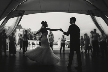Silhouettes of happy bride and groom gently dancing at wedding reception. Gorgeous wedding couple...