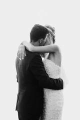 Gorgeous wedding couple of newlyweds embracing while having first dance on white background. Happy bride and groom gently dancing and kissing at wedding reception.