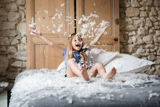 Happy little girl playing with stuffing from a feather pillow