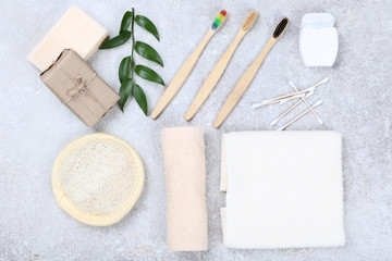Bamboo toothbrushes with washcloth, soap, dental floss and towel on grey background