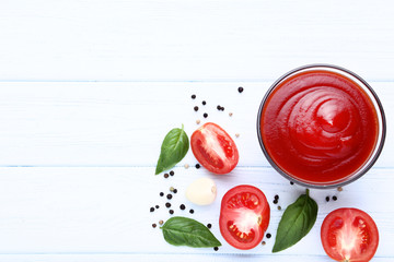 Ketchup in bowl with basil leafs and spices on wooden table
