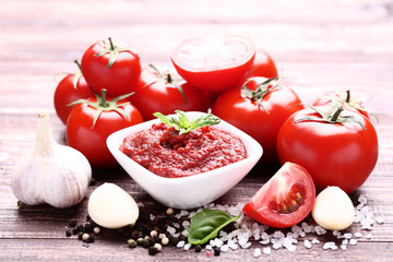 Ketchup in bowl with spices and garlic on brown wooden table