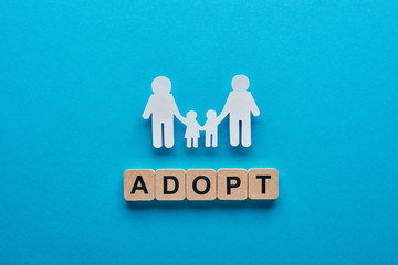 top view of paper cut gay family holding hands on blue background with adopt lettering on wooden...