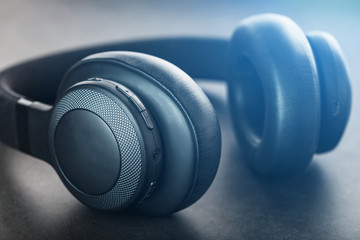 Obraz na płótnie Canvas Wireless black headphones on a dark background with blue and orange backlight. On-ear headphones for playing games and listening to music tracks
