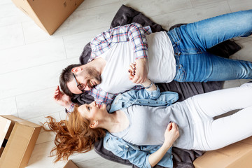 Young couple lying at the floor in empty room with unpacked boxes all arround