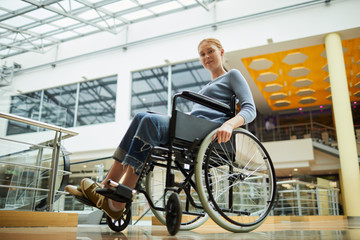 Portrait of young red-haired woman sitting in wheelchair and looking at camera she is going for...