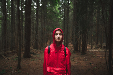 Portrait of attractive girl in red raincoat and hood stands in the evening in the forest on the...