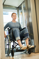 Fototapeta na wymiar Red-haired young woman sitting in wheelchair and moving down the elevator at the hospital